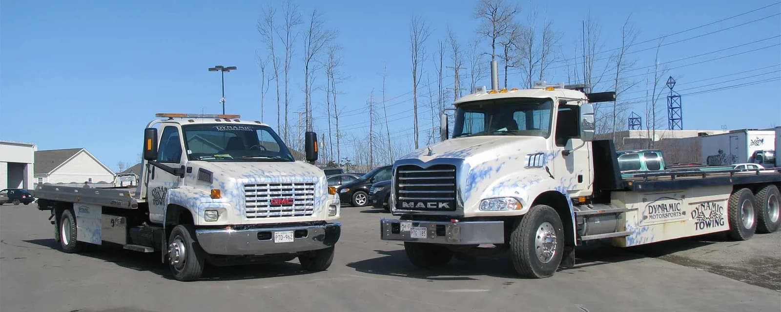 Two Dynamic Towing flat-deck trucks parked side by side, a GMC and a Mack